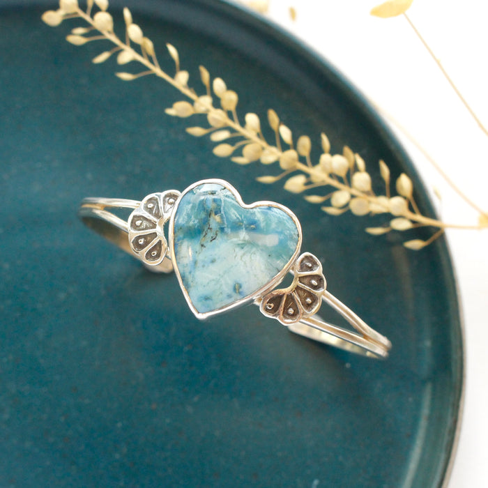 The turquoise heart cuff bracelet styled on a blue plate with dried grass