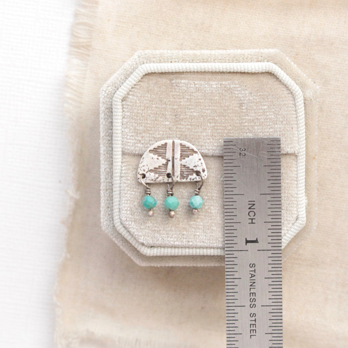 A turquoise pakal arch post earring next to a ruler for size reference
