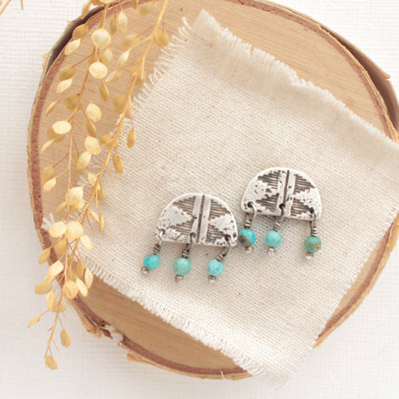 The turquoise pakal arch post earrings styled on wood with linen and dried grass