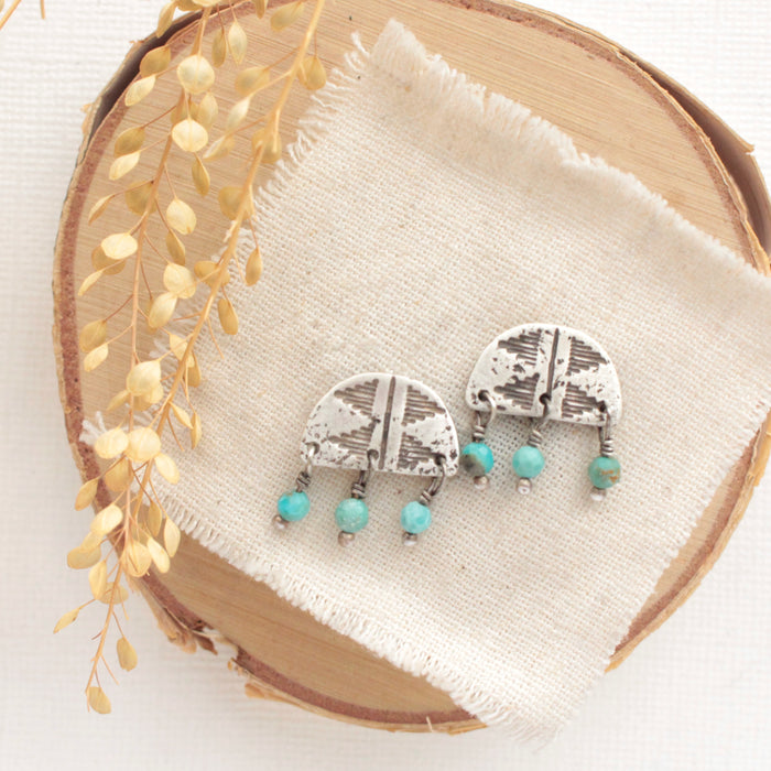 The turquoise pakal arch post earrings styled on wood with linen and dried grass