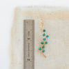 A turquoise wrapped gold vine earring next to a ruler for size reference