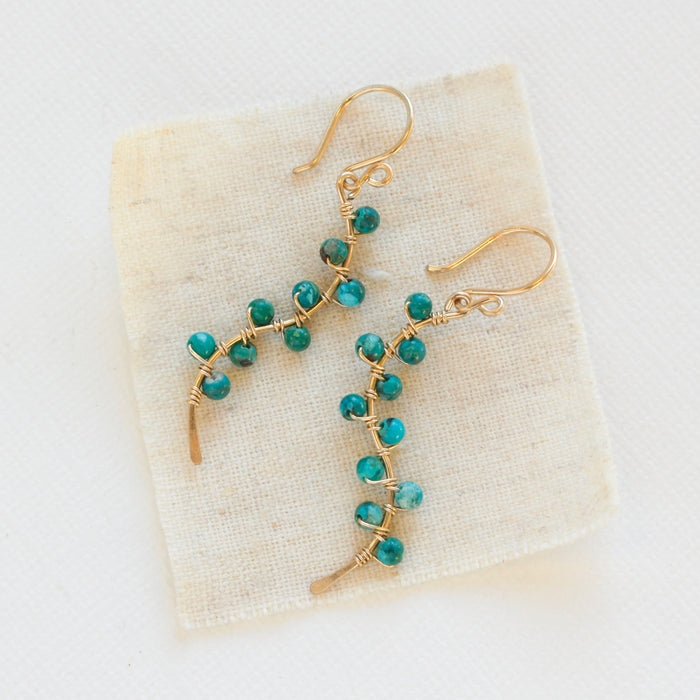 The turquoise wrapped gold vine earrings styled on tan linen