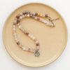 The layered cactus flower violet jade necklace styled on a tan plate to show the adjustable lobster clasp closure