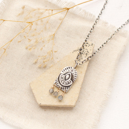 The wanderer arch mixed metal labradorite necklace styled on a tan rock with linen and dried grass