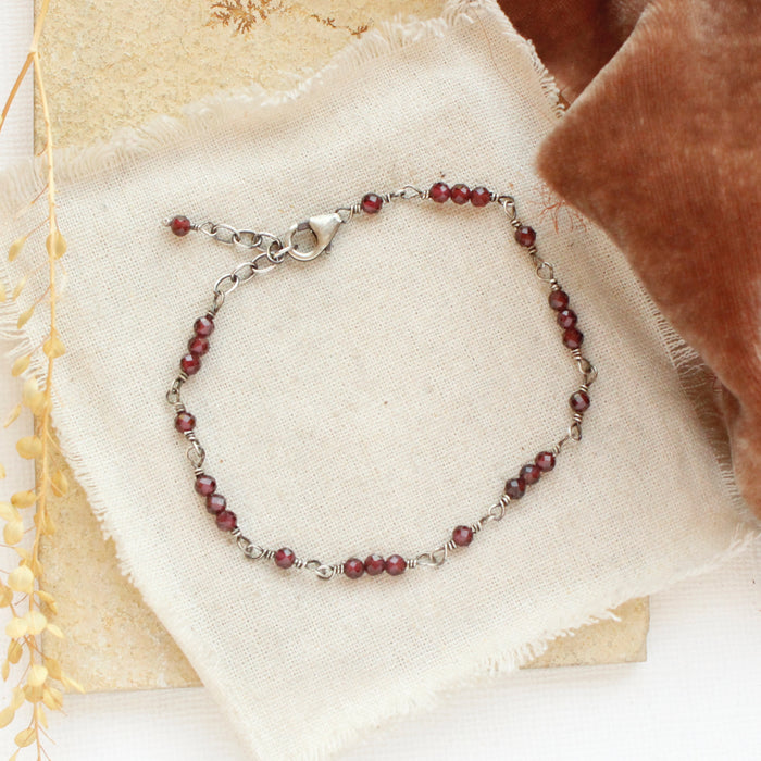 The wrapped garnet bracelet styled on a tan rock with linen, orange velvet, and dried grass