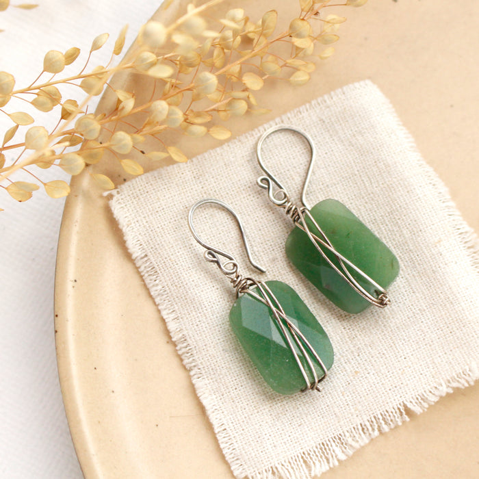 The wrapped green aventurine earrings styled on a tan plate with linen and dried grass