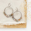 The wrapped rainbow agate hoop earrings styled on a tan rock with linen and dried grass