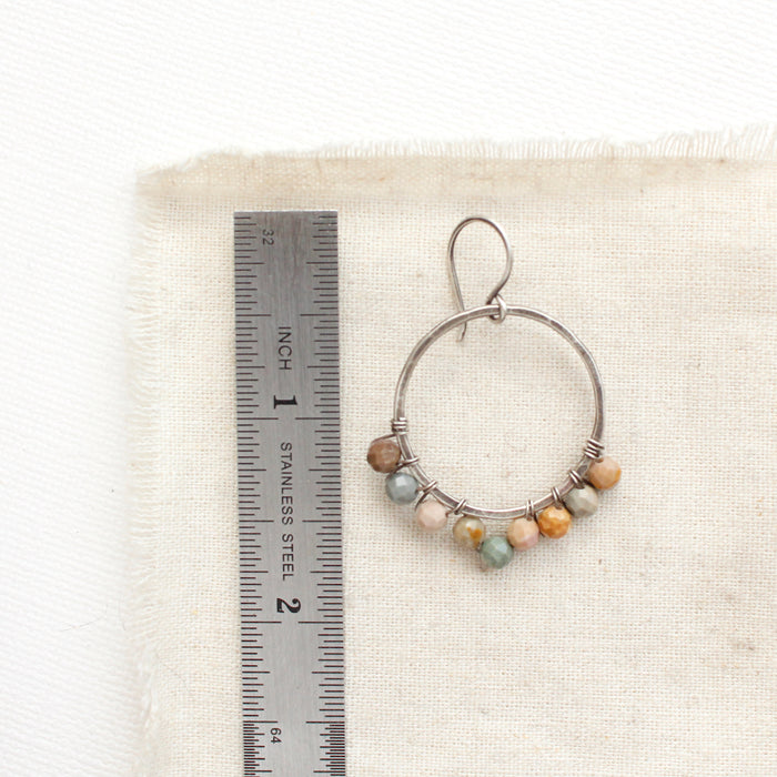 A wrapped rainbow agate hoop earring next to a ruler for size reference