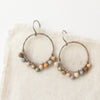 The wrapped rainbow agate hoop earrings styled on tan linen