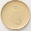 The wrapped silver rainbow necklace styled on a tan plate to show the adjustable lobster clasp closure