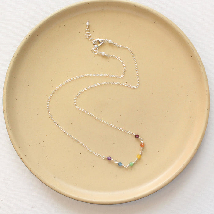 The wrapped silver rainbow necklace styled on a tan plate to show the adjustable lobster clasp closure