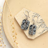 The wrapped snowflake obsidian earrings styled on a tan plate with dried grass