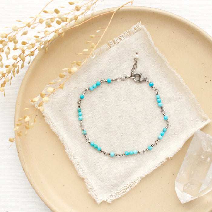 The wrapped turquoise bracelet styled on a tan plate with linen, a crystal, and dried grass