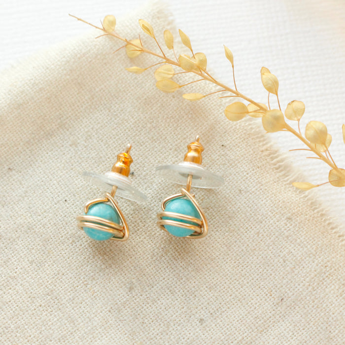 The gold wrapped turquoise post earrings styled on linen with dried grass