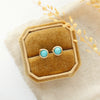 The wrapped turquoise gold post earrings styled on a yellow velvet box with linen and dried grass