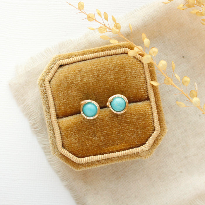 The wrapped turquoise gold post earrings styled on a yellow velvet box with linen and dried grass