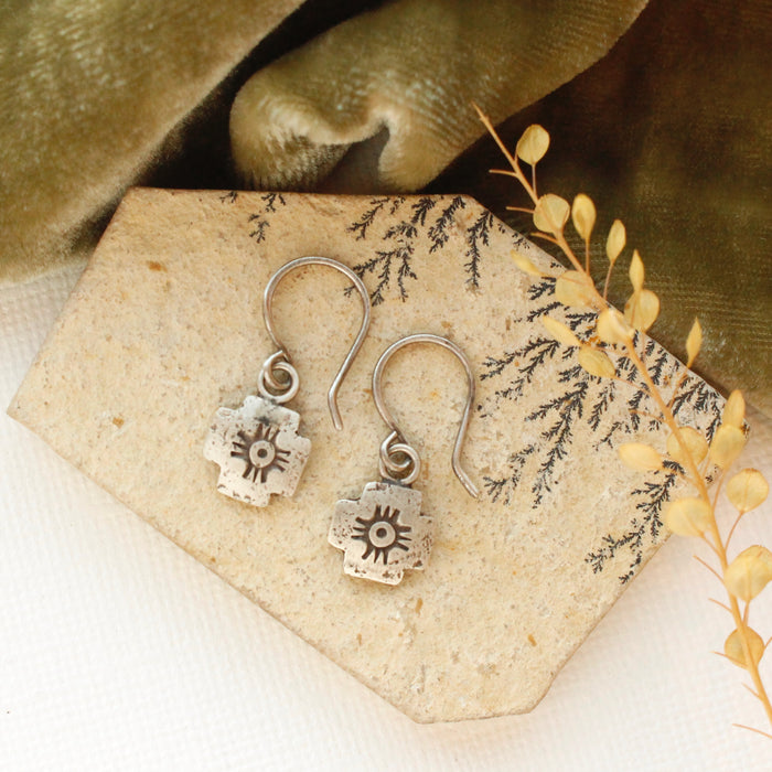 The zuni cross earrings styled on a tan rock with green velvet and dried grass