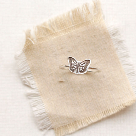 The silver butterfly stacking ring styled on tan linen
