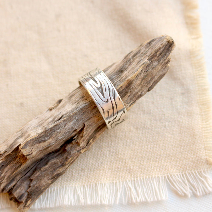 The woodgrain texture band ring styled on a stick on tan linen