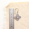 A stamped silver talara earring next to a ruler for size reference