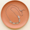 The asmi 5 collar necklace styled on a red plate to show the adjustable clasp chain