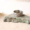 The embrace the chaos stamped band ring styled on a stone and tan linen