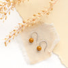 The mookaite lobe hugger earrings styled on tan linen, paper, and dried grass