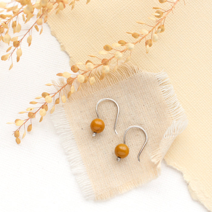 The mookaite lobe hugger earrings styled on tan linen, paper, and dried grass