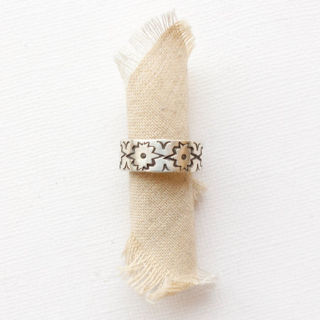 The stamped silver arabesque band ring styled on rolled tan linen