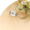 The stamped linear and cross band ring is styled on a tan plate with an air plant
