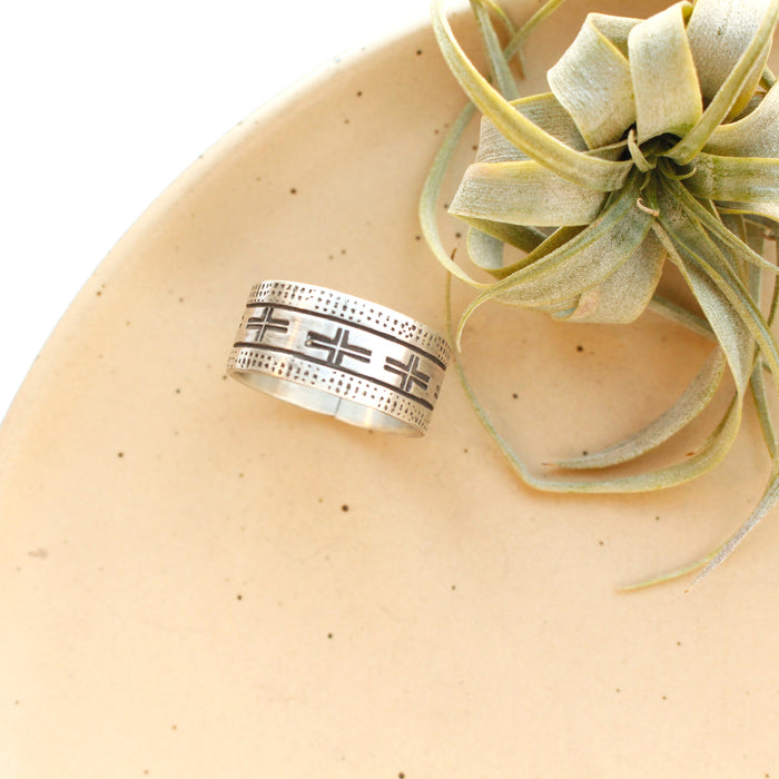 The stamped linear and cross band ring is styled on a tan plate with an air plant
