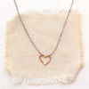 Mixed metal floating heart necklace styled on tan linen