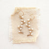 Small white pearls wrapped on gold vines earrings styled on tan linen.