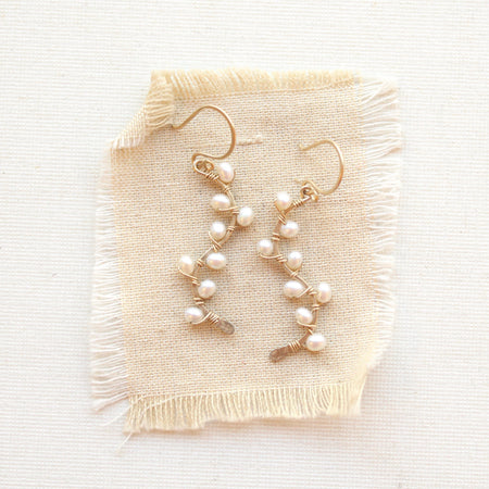 Small white pearls wrapped on gold vines earrings styled on tan linen.