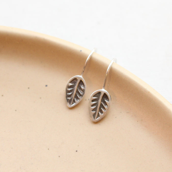 The little leaf lobe hugger earrings styled on a tan plate