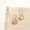 The gold raw silk disc earrings styled on tan linen