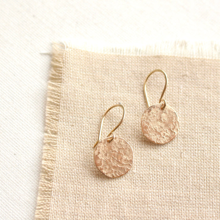 The gold raw silk disc earrings styled on tan linen