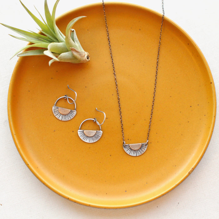 The happy half sun necklace styled on a yellow plate with the matching earrings and an air plant