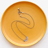 The happy half sun necklace styled on a yellow plate to show the adjustable lobster clasp closure