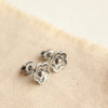 The mini cactus flower post earrings styled on tan linen