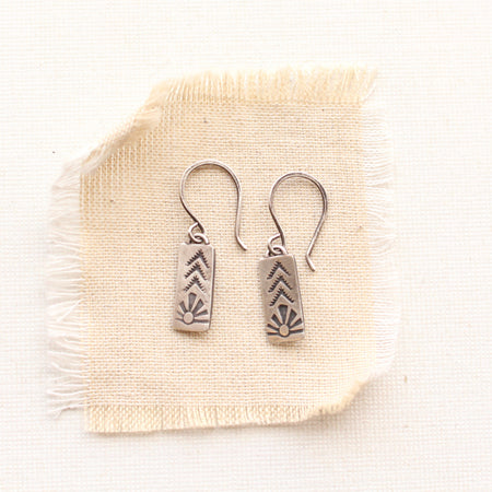 The mini sun bar earrings styled on tan linen