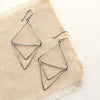 The oxidized silver triple triangle hoop earrings styled on tan linen
