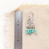 A pakal arch turquoise earring next to a ruler for size reference