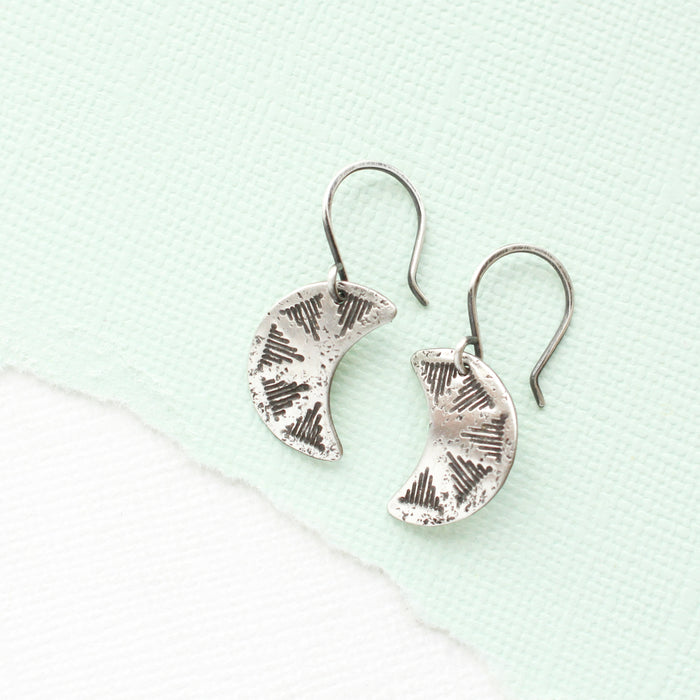 The pakal moon earrings styled on mint colored paper