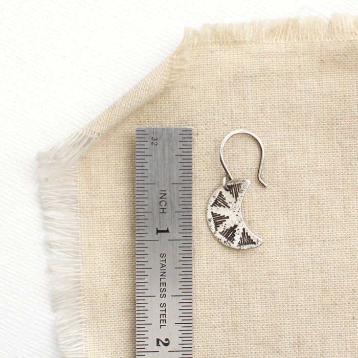 A pakal moon earring next to a ruler for size reference