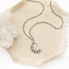 The pakal moon necklace styled on tan linen with a crystal