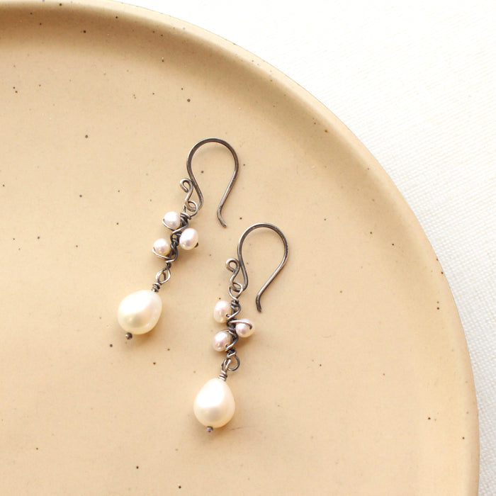 The oxidized silver pearl bud vine earrings styled on a tan plate