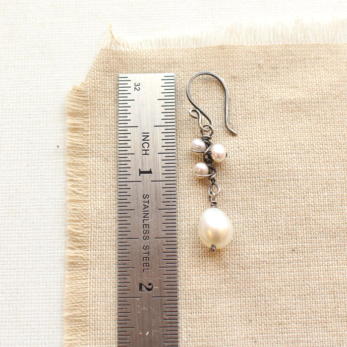 An oxidized silver pearl bud vine earring next to a ruler for size reference