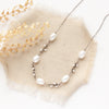 The oxidized silver pearl bud vine necklace styled on tan linen with dried grass