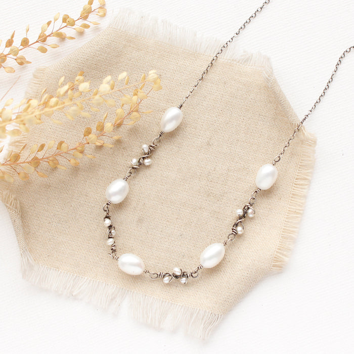 The oxidized silver pearl bud vine necklace styled on tan linen with dried grass